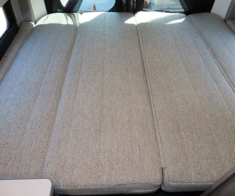 Spacious RV rental sleeping area featuring three light-colored, textured fabric mattress sections for comfort.