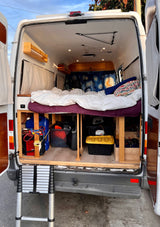 Inside an RV rental camper van: raised bed, ample under-bed storage, Starry Night decor, and ladder access.