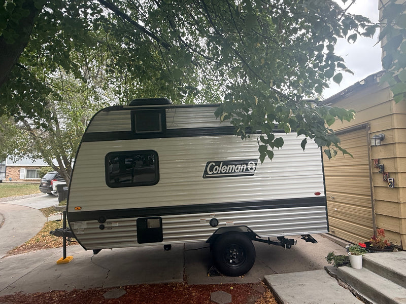 A Coleman travel trailer (RV rental) parked in a driveway under a tree, ready for your next camping adventure. — photo 9
