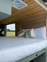 Experience comfort in this RV rental: a spacious bed with cozy pillows, wood paneling, and a beautiful natural view.
