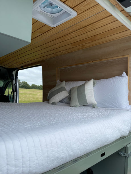Experience comfort in this RV rental: a spacious bed with cozy pillows, wood paneling, and a beautiful natural view.
