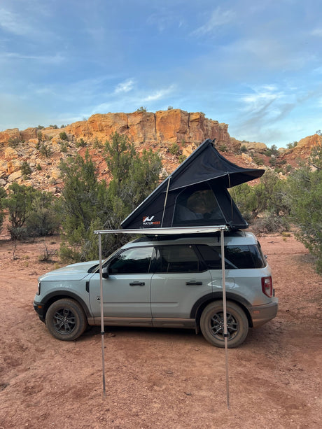 Rooftop tent on SUV at desert campsite by cliffs. Great RV rental option for your next outdoor adventure.