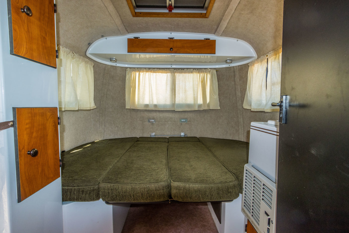 Inside a cozy RV rental: green cushioned bed/seating area, windows, cabinets, & AC unit.