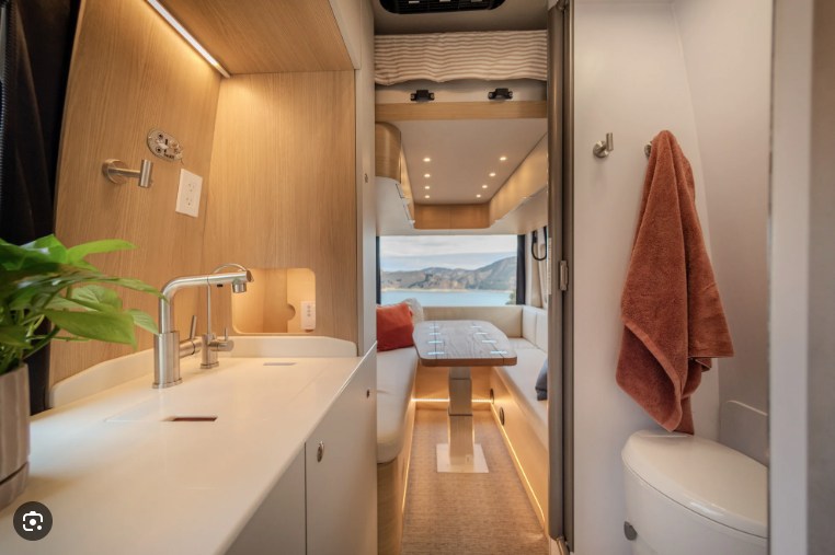 RV rental's modern interior: kitchen, dining with scenic window view, and compact bathroom. Ideal for stylish travel.