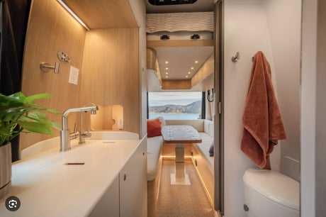 RV rental's modern interior: kitchen, dining with scenic window view, and compact bathroom. Ideal for stylish travel.