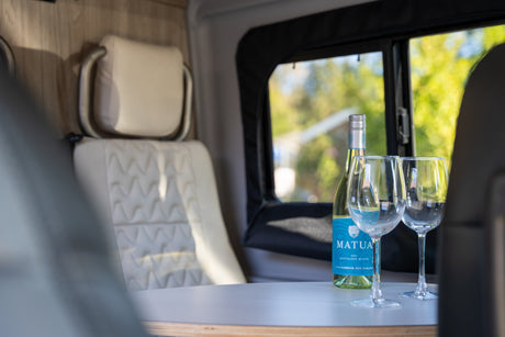 A bottle of Matua Sauvignon Blanc wine and two glasses are on a table inside a comfortable RV rental, ready for relaxation.