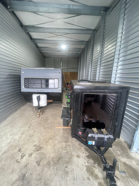 Grey camper and black enclosed trailer in indoor storage, ideal for an RV rental or hauling needs.