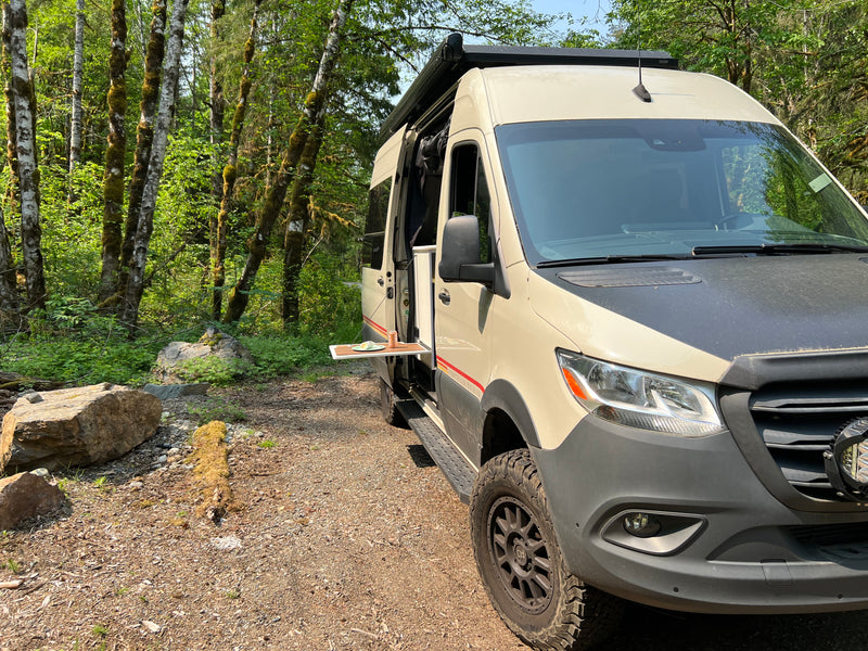 Explore nature with an RV rental! This camper van is parked in a lush forest with a side table extended for a meal. — photo 9