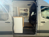 Explore van life with this RV rental! Interior view from the open side door shows custom kitchen, flooring, and seating.