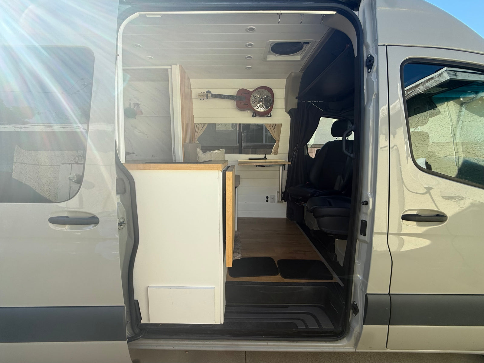 Explore van life with this RV rental! Interior view from the open side door shows custom kitchen, flooring, and seating.