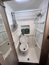 Inside an RV rental: a compact wet bath with a toilet, shower, towels, drying rod, and mirrored door.