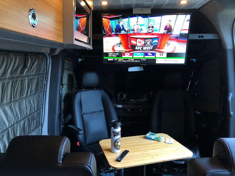 Cozy rv rental interior with a big screen TV showing sports, swivel chairs, and a small table. Ideal for travel entertainment. — photo 5