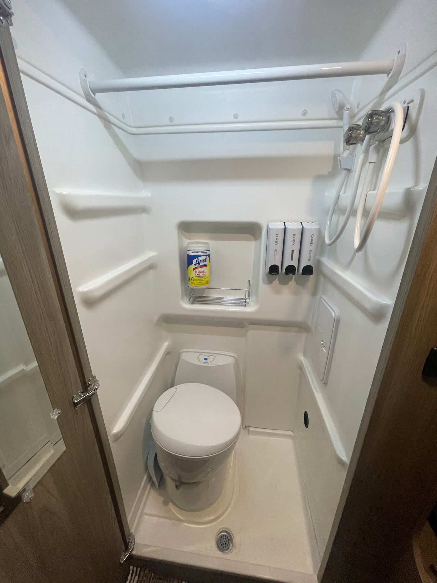 Compact rv rental bathroom with integrated shower, toilet, and wall-mounted dispensers for essentials.