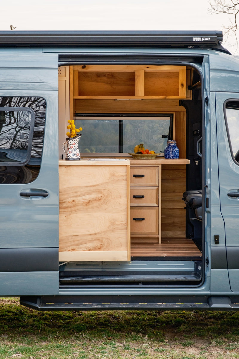 Explore this RV rental! A blue camper van with its sliding door open, revealing a custom wooden kitchen and comfortable interior. — photo 3