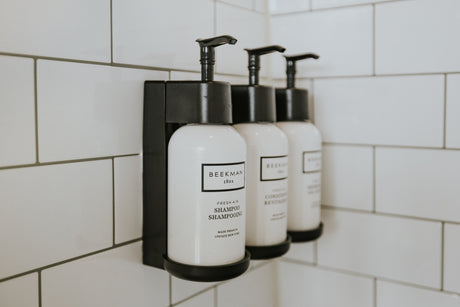 RV rental bathroom comfort: Wall-mounted Beekman 1802 shampoo & conditioner dispensers on white subway tile.
