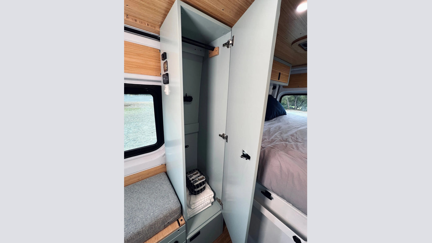 RV rental van interior features an open closet with towels, a bed, and a window view. Includes storage and seating.