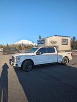 A white Ford F-150 truck with a Scout camper, ideal for an rv rental adventure in snowy mountains.