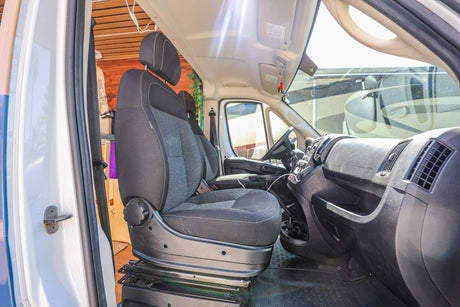Experience our RV rental! The front cabin of a camper van conversion, featuring a comfortable swivel driver's seat, ready for the road.
