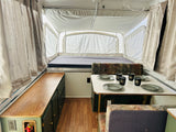 Inside a bright pop-up rv rental, featuring a bed, dining table with dishes, and cabinet storage.