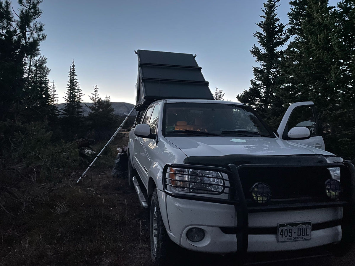 White overland truck with a rooftop tent, perfect for an RV rental adventure, parked amidst evergreen trees at twilight. — photo 4
