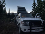 White overland truck with a rooftop tent, perfect for an RV rental adventure, parked amidst evergreen trees at twilight.