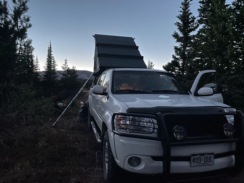 White overland truck with a rooftop tent, perfect for an RV rental adventure, parked amidst evergreen trees at twilight. — photo 4