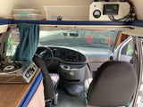 Inside a compact RV rental camper van, showing the cockpit, a stove, overhead storage, and solar power setup.