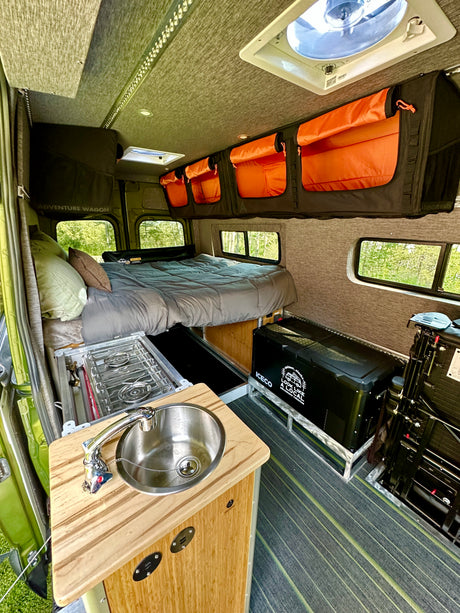 Adventure Wagon RV rental: comfy bed, compact kitchen w/ sink, stove & cooler. Ready for travel.