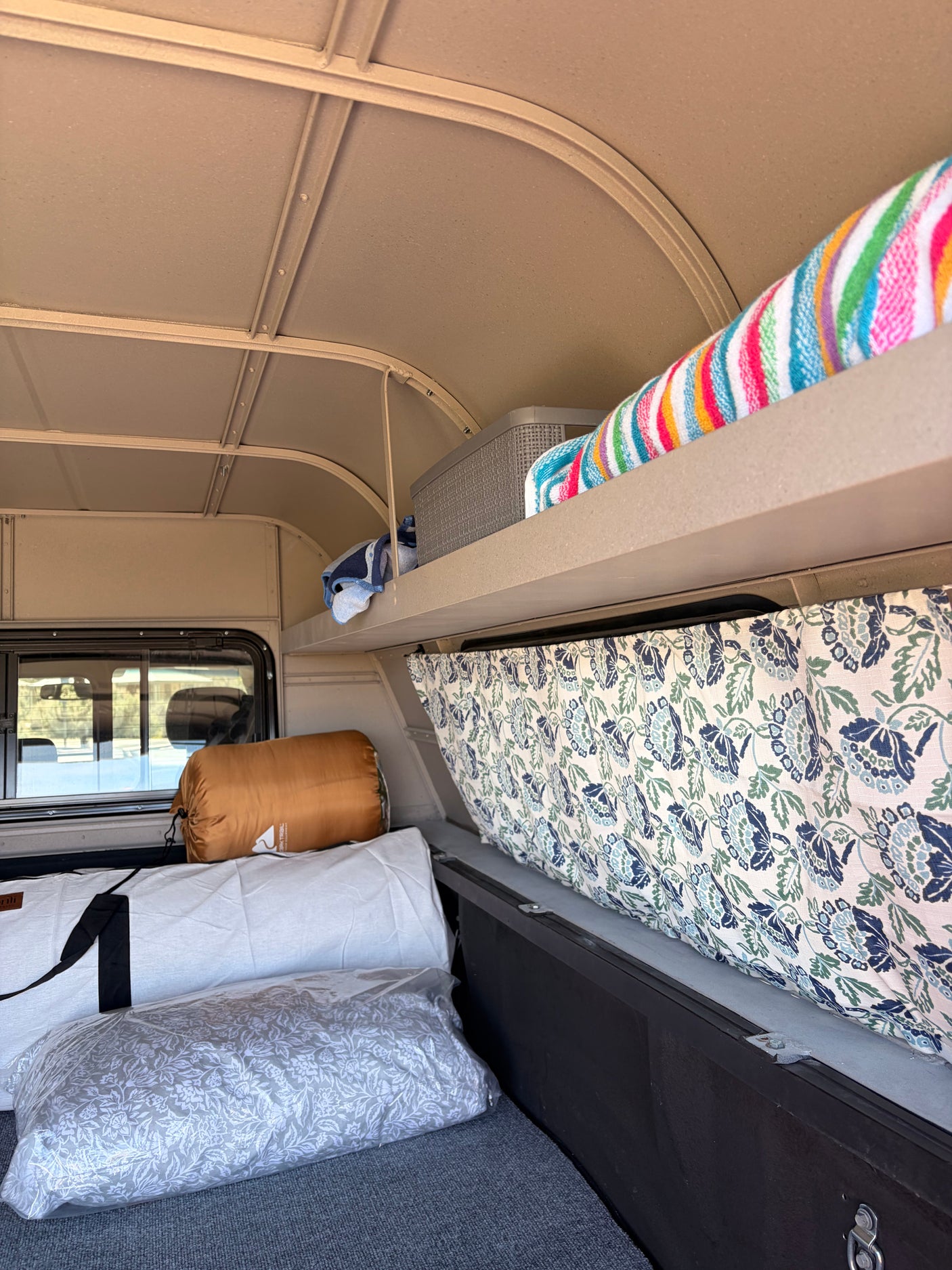 Cozy camper interior for your next rv rental adventure, featuring a bed, storage shelf, and patterned curtain.