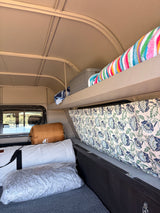 Cozy camper interior for your next rv rental adventure, featuring a bed, storage shelf, and patterned curtain.