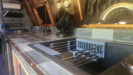 RV rental kitchen: compact sink with drying rack, fan, cooktop, and tiled counter. Ready for your mobile adventures.