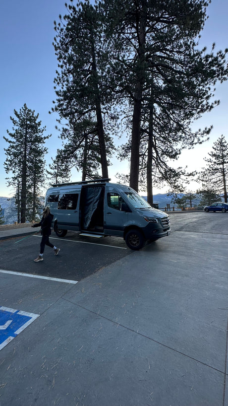 Gray Mercedes Sprinter rv rental camper van parked in a mountain forest. Person walks nearby.
