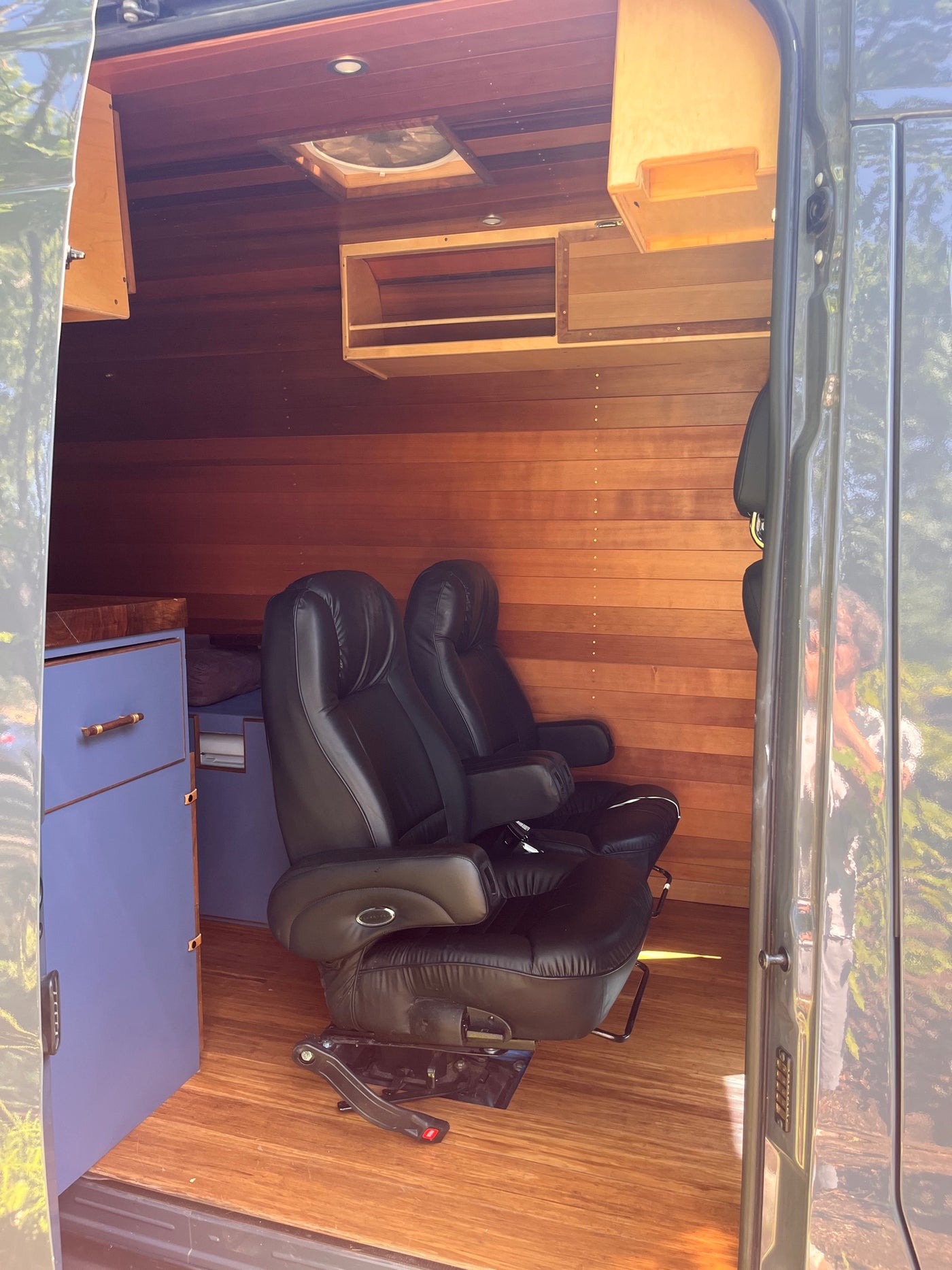 Cozy, custom RV rental interior featuring warm wood walls/flooring, two plush black leather chairs, and cabinetry. — photo 9