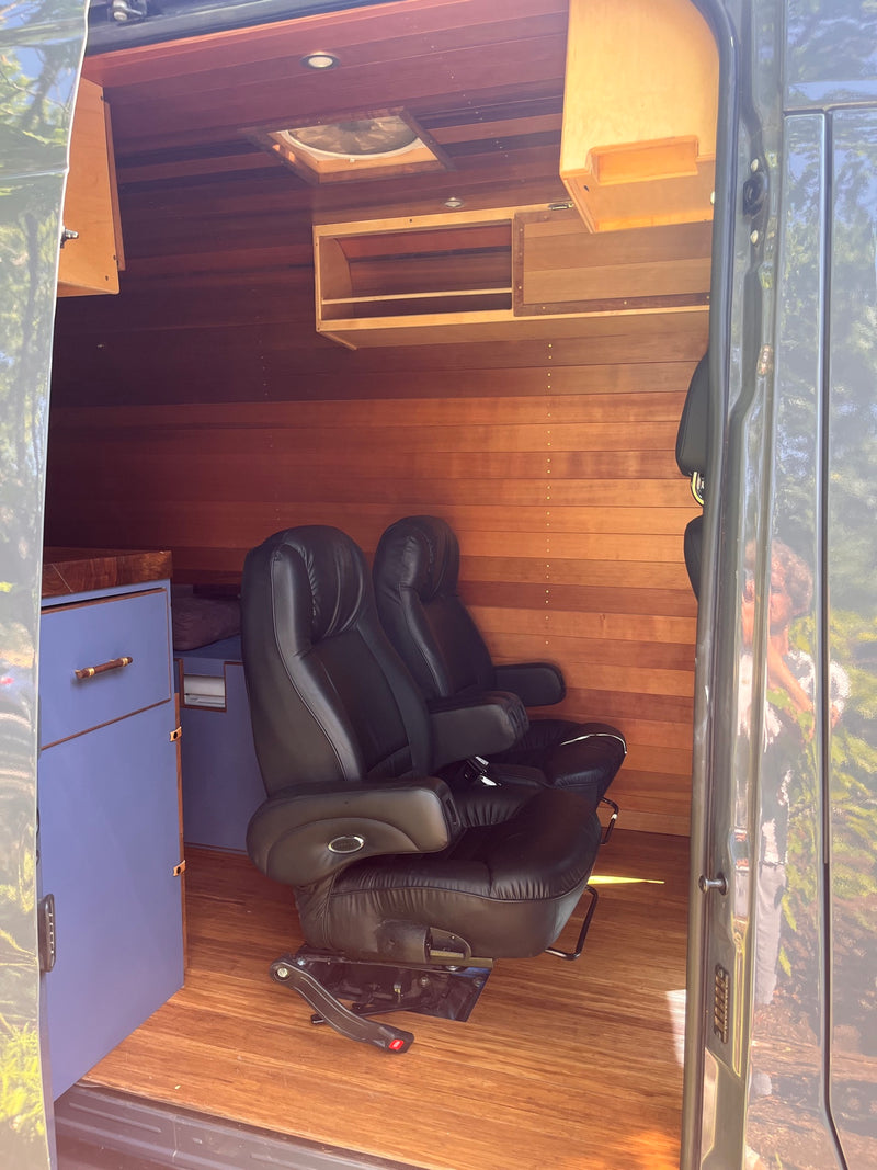 Cozy, custom RV rental interior featuring warm wood walls/flooring, two plush black leather chairs, and cabinetry. — photo 9