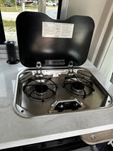 This rv rental features a compact stainless steel two-burner stove, ideal for cooking meals in your camper kitchen.