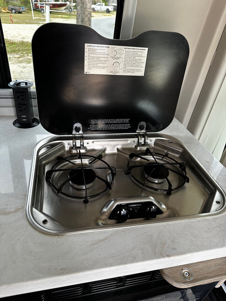 This rv rental features a compact stainless steel two-burner stove, ideal for cooking meals in your camper kitchen.