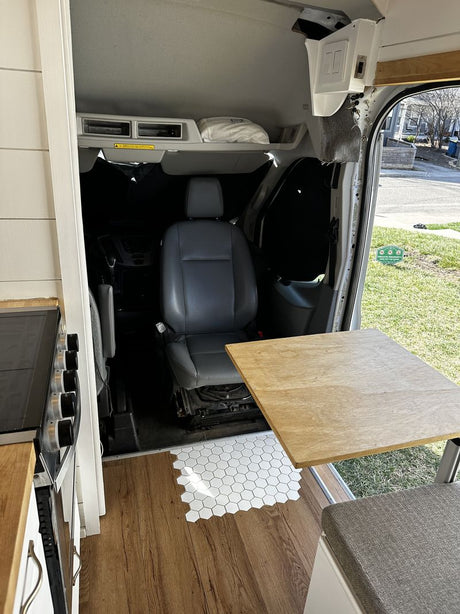 RV rental custom interior: kitchen counter, wood & hex tile flooring, swiveling passenger seat, table, and bench.