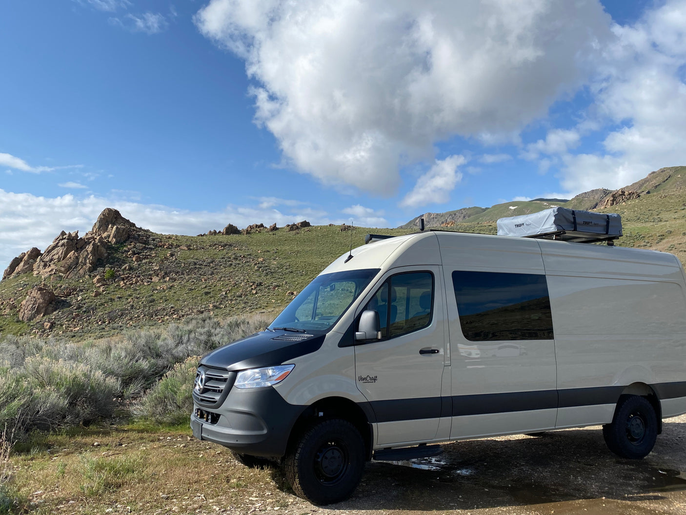 Beige Sprinter campervan with rooftop tent, ideal for RV rental, parked in a rocky mountain landscape.