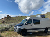 Beige Sprinter campervan with rooftop tent, ideal for RV rental, parked in a rocky mountain landscape.