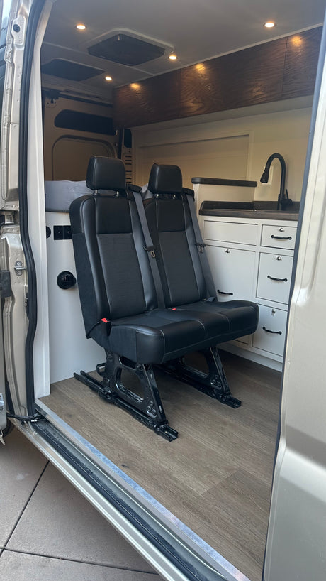 Modern RV rental camper van interior featuring two rear passenger seats, a kitchen area, and a bed.