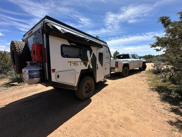 Experience adventure with this Teton off-road rv rental camper, hitched to a truck on a dirt trail under blue skies. — photo 2