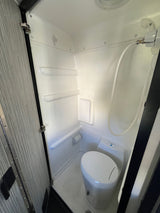 Explore this clean, compact RV rental wet bath, featuring a white toilet, shower hose, and built-in shelves.