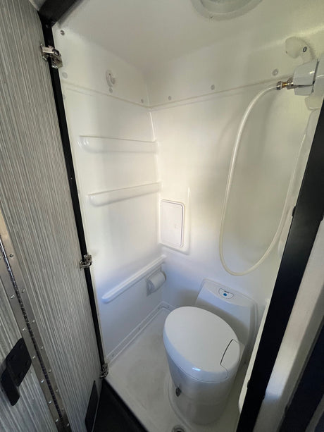 Explore this clean, compact RV rental wet bath, featuring a white toilet, shower hose, and built-in shelves.