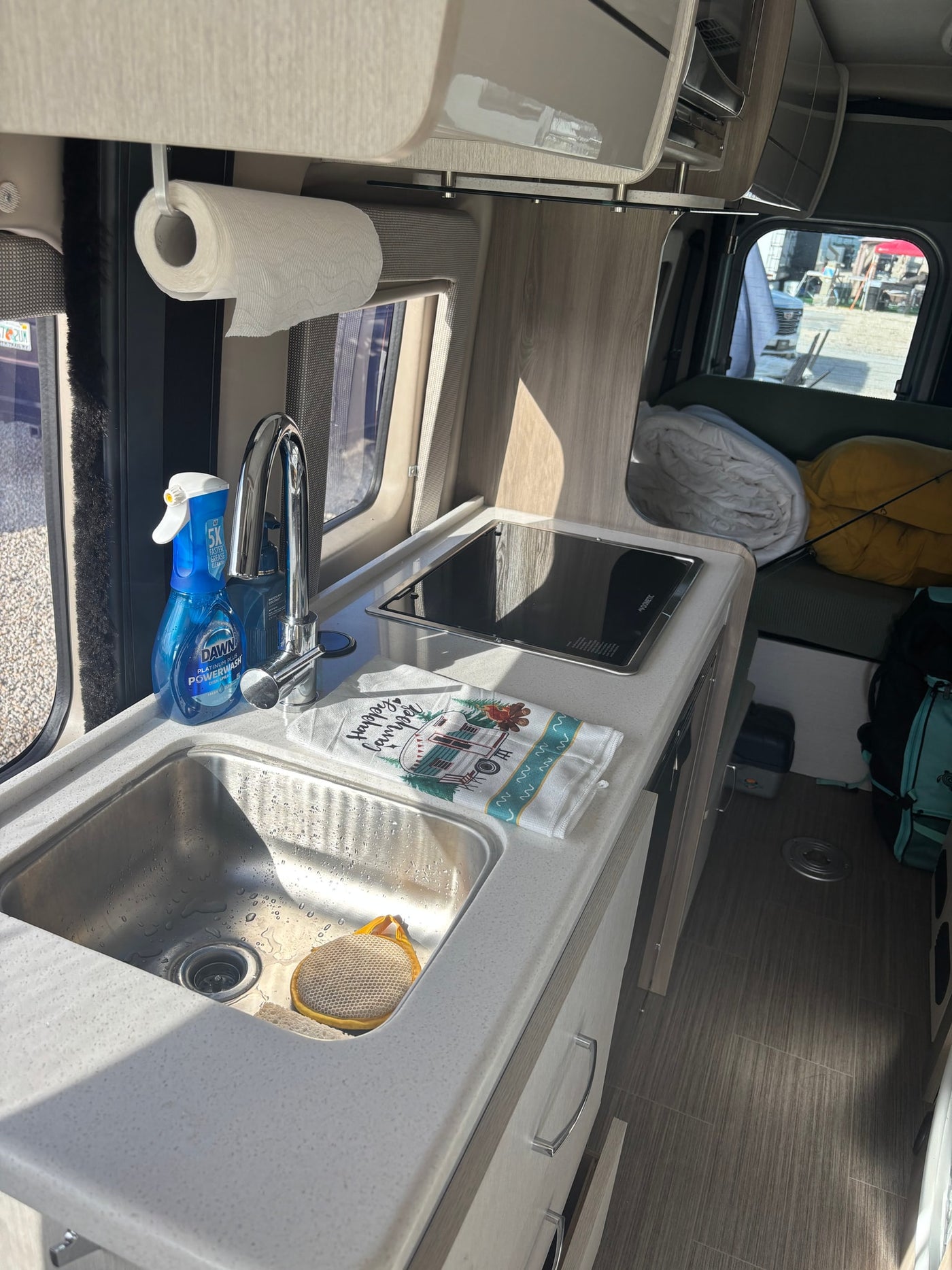 This rv rental features a compact kitchen with a sink, stovetop, and essentials like dish soap & paper towels. — photo 3