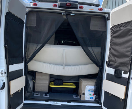 Rear view of an RV rental camper van with open doors, revealing a mesh insect screen, bed, and under-bed storage.