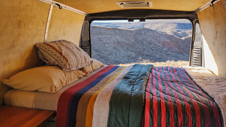 Cozy RV rental bed looking out to vast mountains. Enjoy nature from your comfortable camper van conversion.