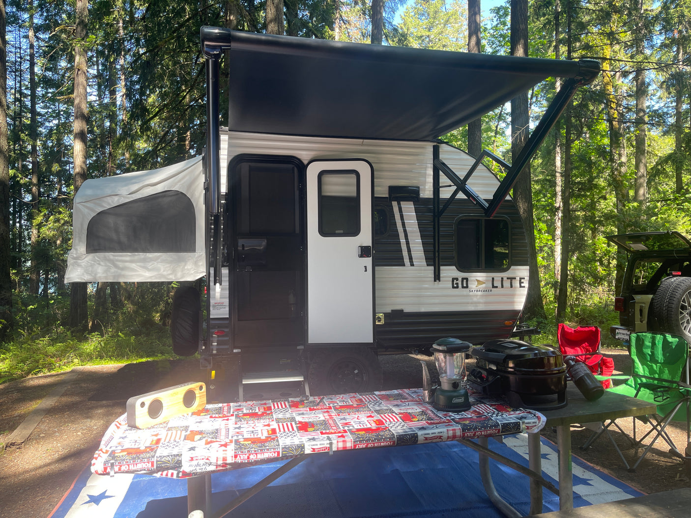 Enjoying an RV rental adventure! Go-Lite travel trailer with extended awning & pop-out tent in a shaded forest campsite.