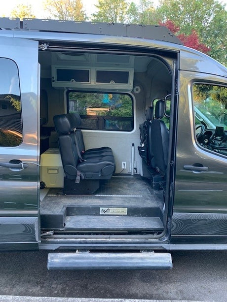 Accessible gray RV rental van with open side door showing spacious interior, passenger seats, overhead storage, and a platform floor.
