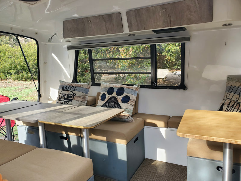 Bright RV rental interior features two tables, comfy dinette seating, and large windows overlooking green scenery. — photo 18