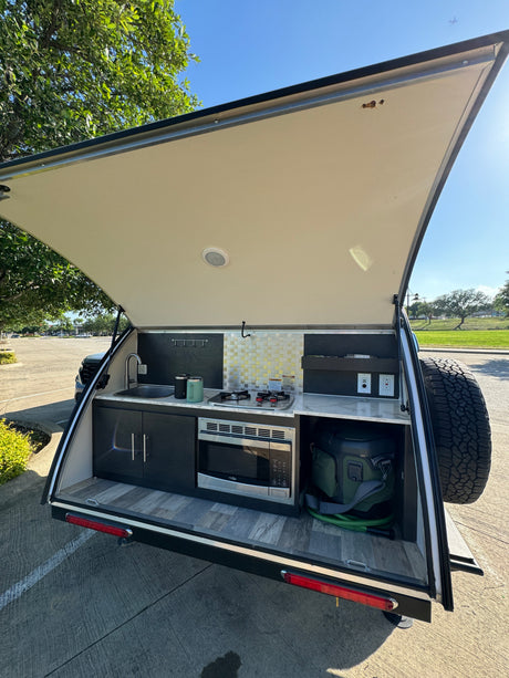 RV rental's outdoor kitchen, featuring a sink, stove, microwave, and cooler for open-air cooking adventures.